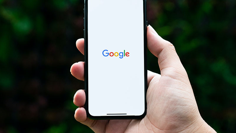 Hand holding phone with the Google home page open on the screen.